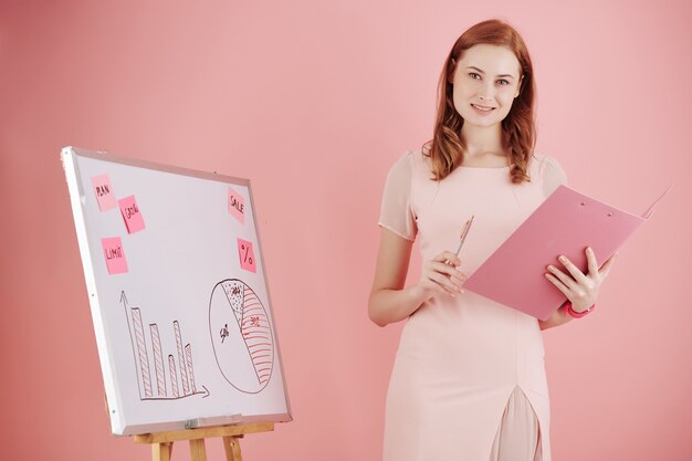 Porträt der fröhlichen jungen Geschäftsfrau, die am Whiteboard steht, wenn Präsentation für Kollegen durchführt