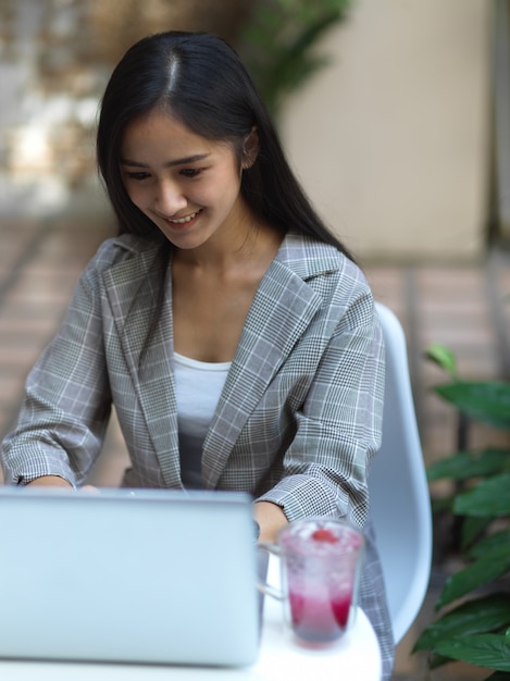 Porträt der Geschäftsfrau, die am Laptop auf Couchtisch mit Getränk im Garten arbeitet