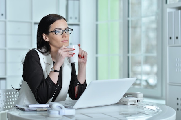 Porträt der Geschäftsfrau, die im Büro mit einer Tasse Tee arbeitet