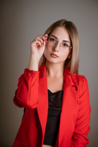 Porträt der Geschäftsfrau mit blonden Haaren in einer roten Jacke passt ihre Brille an