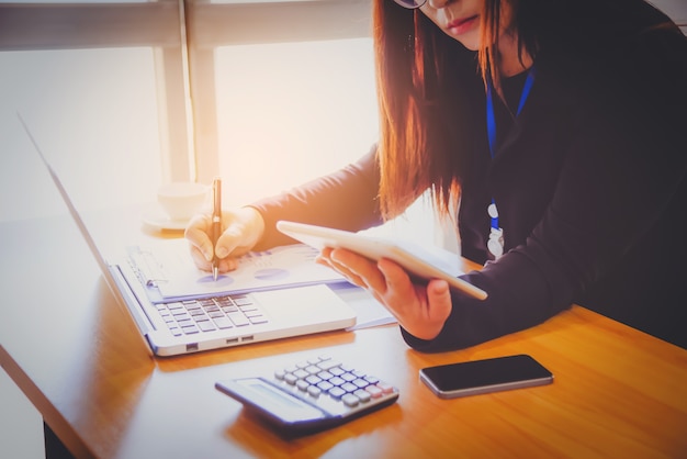 Porträt der Geschäftsfrau mit Laptop, Finanzdiagramm und schreibt auf ein Dokument in ihrem Büro.