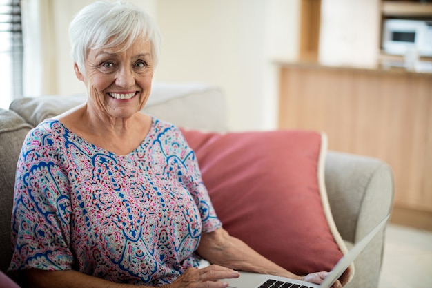 Porträt der glücklichen älteren Frau, die Laptop im Wohnzimmer zu Hause verwendet