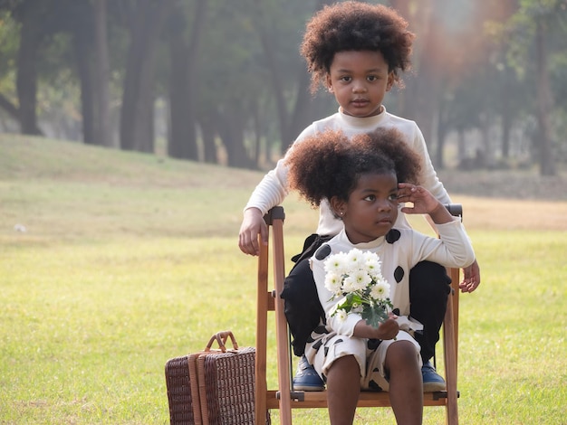 Porträt der glücklichen afroamerikanischen Jungen und Mädchen, die am schönen Morgen einen Picknicktisch im Garten setzen Abenteuer-Kindergarten-Tagesausflug in die wilde NaturxA