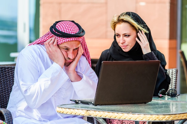 Porträt der glücklichen arabischen Geschäftsfrau und des Geschäftsmanns im tropischen Sommercafé. Freiberufliche und Fernarbeit. Verliebte arabische Frau und arabisches Mannpaar arbeiten zusammen am Ufer