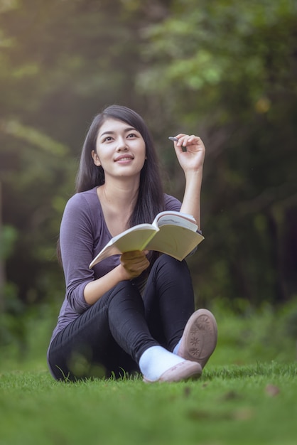 Porträt der glücklichen charmanten asiatischen Frau, die ein Buch im Freien liest