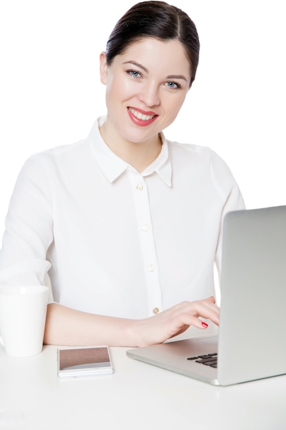 Porträt der glücklichen erfolgreichen attraktiven Brunettegeschäftsfrau im weißen Hemd, das mit Laptop sitzt und mit dem zahnigen Lächeln schaute, erfüllte Gesichtsausdruck. Indoor-Studioaufnahme, isoliert in weißem Hintergrund