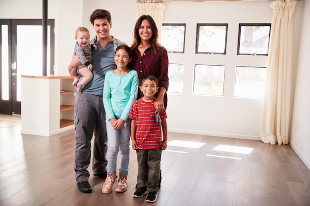 Porträt der glücklichen Familie mit dem Baby, das in der leeren Lounge des neuen Hauses steht