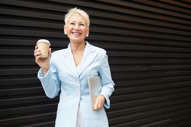 Porträt der glücklichen Frau, die Kaffee an der Gebäudewand trinkt