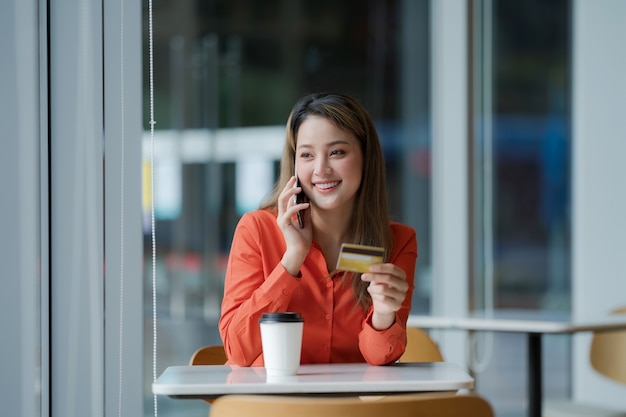 Porträt der glücklichen Frau, die Smartphone mit Kreditkarte und lächelndem Gesicht im kreativen Büro oder im Café am Einkaufszentrum hält