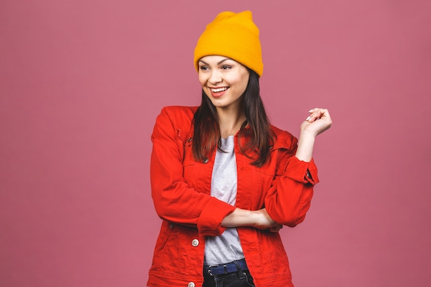 Porträt der glücklichen Hipsterfrau im gelben Hut und im roten Hemd lokalisiert über rosa Wand.