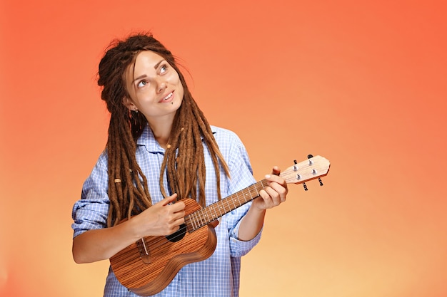 Porträt der glücklichen jungen Frau, die Ukulele spielt