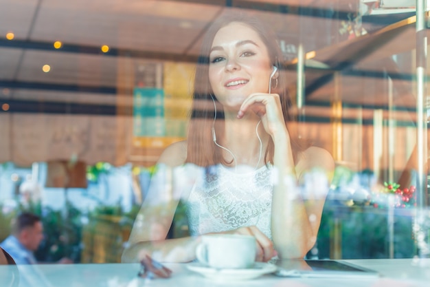 Porträt der glücklichen jungen Geschäftsfrau mit Becher in den Händen Kaffee am Restaurant trinkend