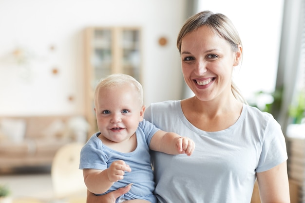 Porträt der glücklichen jungen Mutter, die ihren hübschen Kleinkindsohn lächelnd hält