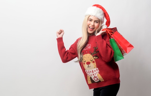 Porträt der glücklichen kaukasischen jungen Frau im Weihnachtsmann-Hut mit Einkaufstaschen über weißem Hintergrund