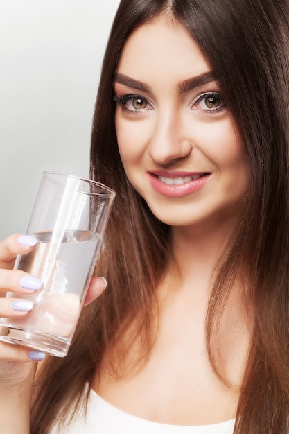 Porträt der glücklichen lächelnden jungen Frau mit Glas Süßwasser.