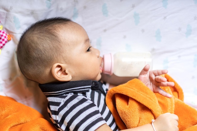 Foto porträt der glücklichen liebesfamilie asiatische mutter, die mit entzückendem kleinen asiatischen baby spieltmutter, die dem süßen sohn in einem weißen schlafzimmer eine flasche milch füttertliebe des familienkonzepts