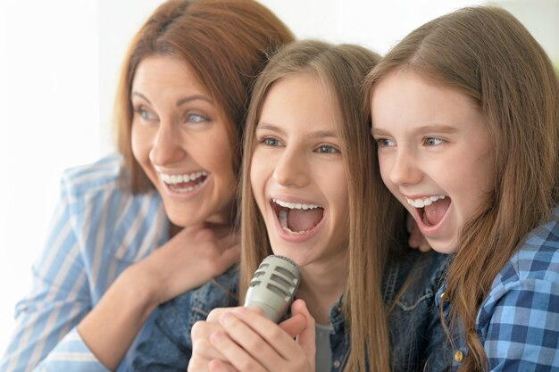 Porträt der glücklichen Mutter und der Töchter, die Karaoke singen