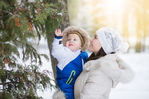 Porträt der glücklichen Mutter und des Babys im Winterpark. Erster Winterschnee und glückliches Familienkonzept. Lebensstil der jungen Mutter und ihres einjährigen Kindes