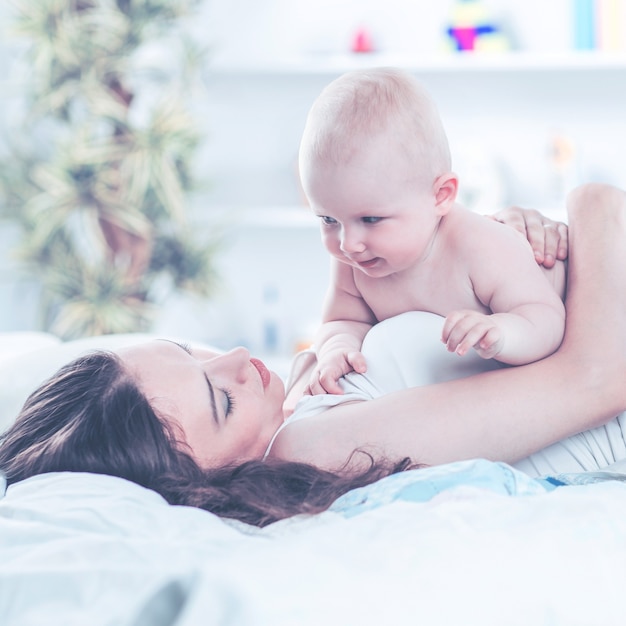 Porträt der glücklichen Mutter und des einjährigen Babys auf dem Bett im Schlafzimmer