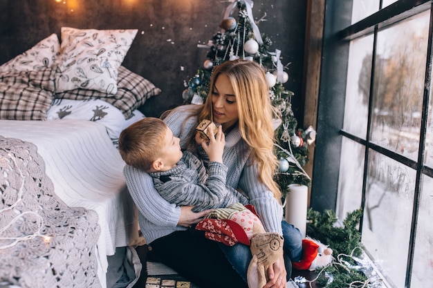 Porträt der glücklichen Mutter und des entzückenden Babys feiern Weihnachten. Neujahrsfeiertage. Kleinkind mit Mutter im festlich geschmückten Raum mit Weihnachtsbaum und Dekorationen.