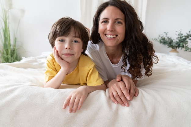 Porträt der glücklichen Mutter und des kleinen Sohns, der am ersten Feiertagsmorgen fröhlich im Bett liegt und sich zusammen entspannt