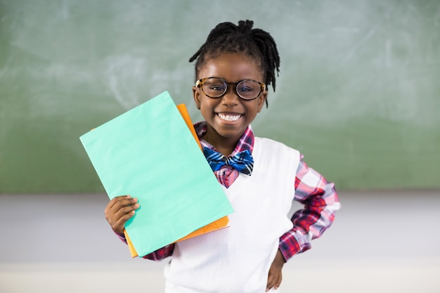 Porträt der glücklichen Schulmädchenholdingdatei im Klassenzimmer