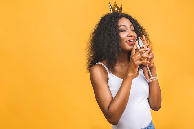 Porträt der glücklichen schwarzen afroamerikanischen Frau mit Glas Champagner und goldener Krone