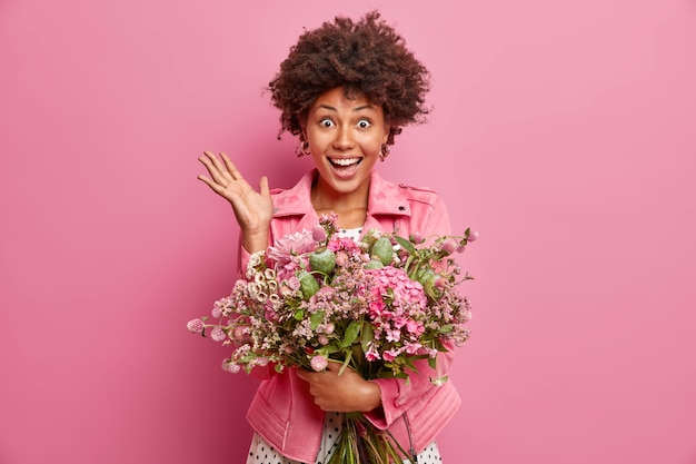 Porträt der gut aussehenden Frau hebt Handfläche reagiert auf unerwartete Glückwünsche hat Datum mit Freund hält großen Blumenstrauß über rosa Wand isoliert