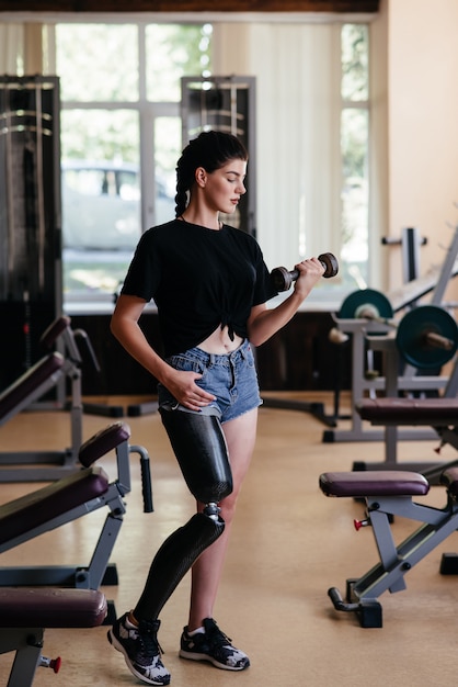 Porträt der gymnastisch behinderten Frau, die Prothese im Trainingsanzugtraining trägt und Langhantel im Fitnessstudio hebt