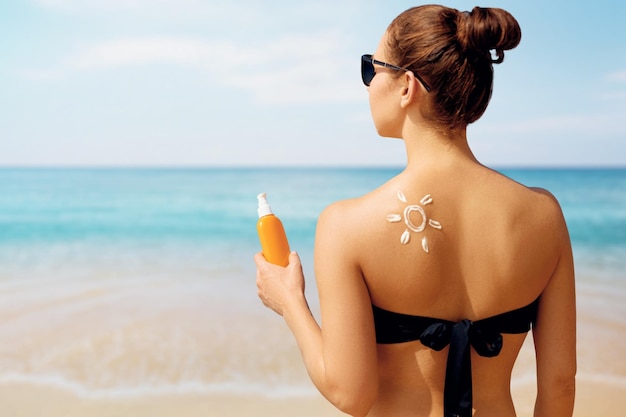 Porträt der herrlichen Frau im Bikini mit der gezeichneten Sonne auf einer Schulter am Strand