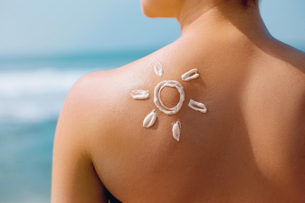 Porträt der herrlichen Frau im Bikini mit der gezeichneten Sonne auf einer Schulter am Strand