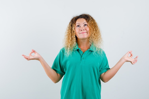 Porträt der hübschen blonden Frau, die Yoga-Geste im grünen Polo-T-Shirt zeigt und optimistische Vorderansicht schaut