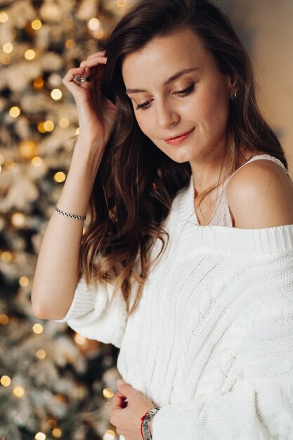 Porträt der hübschen Frau im weißen Kleid der Mode lächelt nahe dem Weihnachtsbaum zu Hause