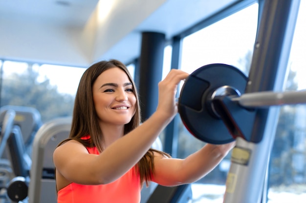 Porträt der hübschen Frau setzt Gewichtsplatte auf den Barbell in Turnhalle ein