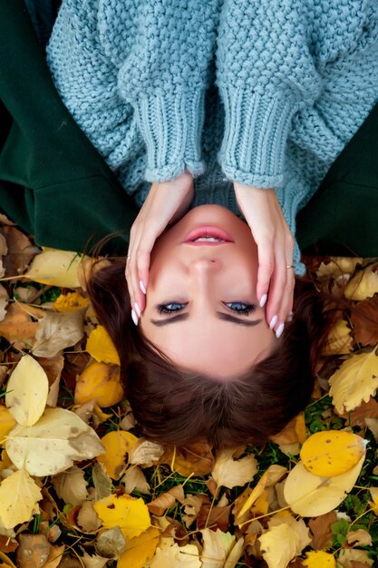 Porträt der hübschen jungen Frau des slawischen Aussehens in der dunklen Freizeitkleidung im Herbst, liegend auf herbstgelben Blättern