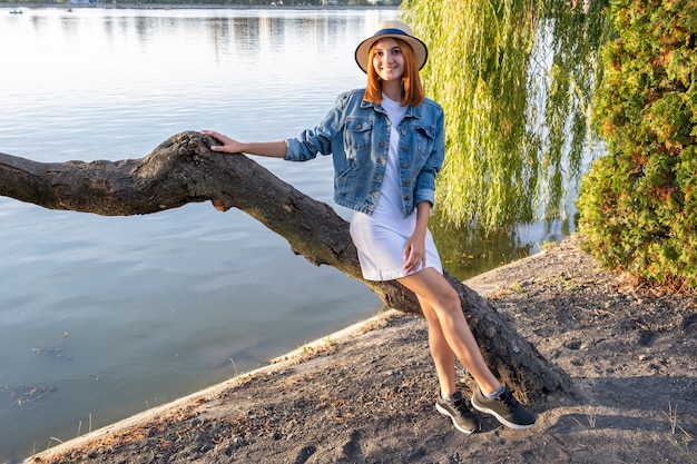 Porträt der hübschen jungen Frau im kurzen Rock der Freizeitkleidung und im Hut im Herbstpark.