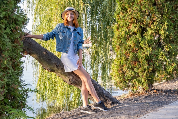 Porträt der hübschen jungen Frau im kurzen Rock der Freizeitkleidung und im Hut im Herbstpark.