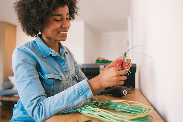 Porträt der jungen Afro-Frau, die Elektrizitätsproblem mit Kabeln am neuen Haus behebt. Reparatur- und Renovierungshauskonzept.