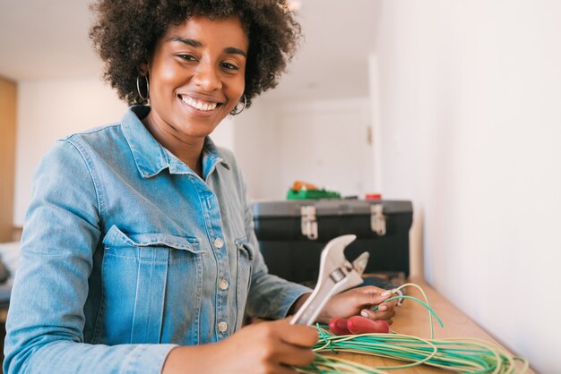 Porträt der jungen Afro-Frau, die Elektrizitätsproblem mit Kabeln am neuen Haus behebt. Reparatur- und Renovierungshauskonzept.