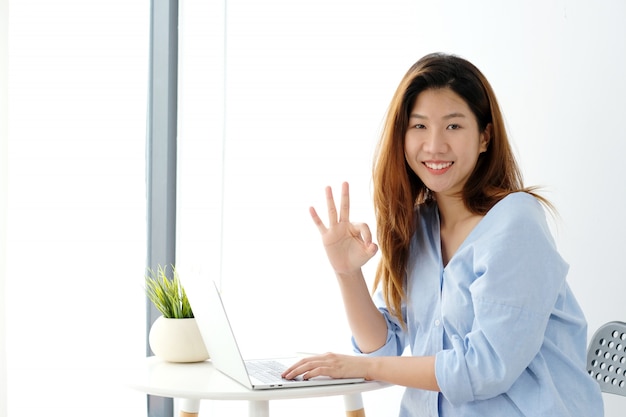 Porträt der jungen asiatischen Frau, die okayhandzeichen zeigt und beim Arbeiten lächelt