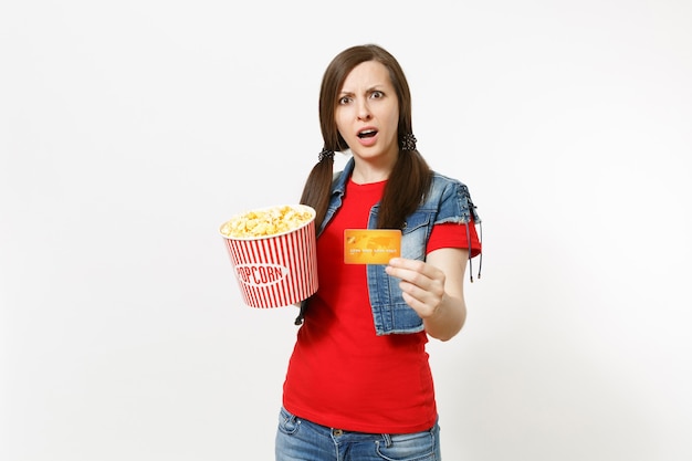 Porträt der jungen betroffenen attraktiven brünetten Frau in Freizeitkleidung, die Filmfilm ansieht, Eimer Popcorn und Kreditkarte halten lokalisiert auf weißem Hintergrund. Emotionen im Kinokonzept.