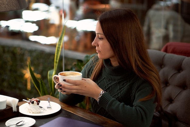 Porträt der jungen brünetten Frau, die Kaffee in einem Café trinkt und Nachtisch isst