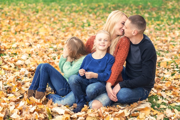 Porträt der jungen Familie, die im Herbstlaub sitzt