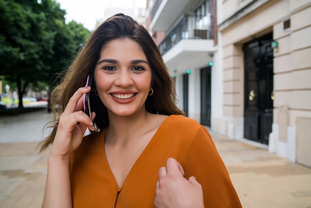 Porträt der jungen Frau, die am Telefon spricht, während sie draußen auf der Straße geht. Stadt- und Kommunikationskonzept.