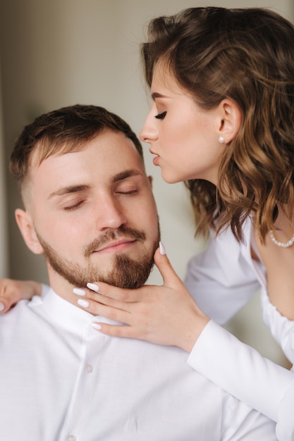 Porträt der jungen Frau, die attraktive Frau des Ehemanns mit ihrer schönen weißen Kleidung des Mannes küsst