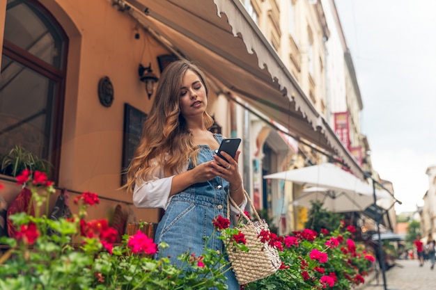 Porträt der jungen Frau, die breit lächelt, während das Smartphone im Freien spaziert