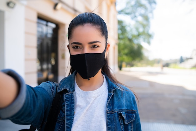 Porträt der jungen Frau, die Gesichtsmaske trägt und Selfies im Freien nimmt