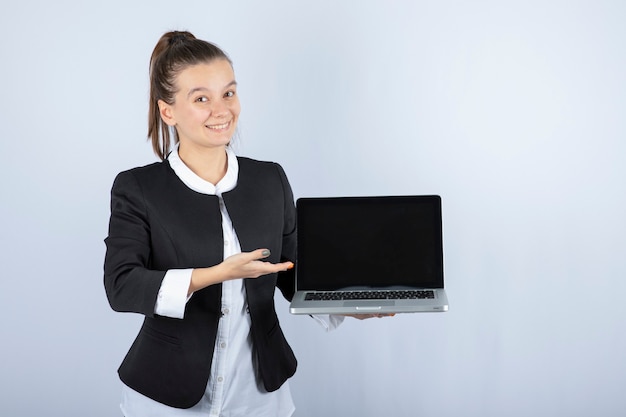 Porträt der jungen Frau, die Laptop über weißer Wand hält.