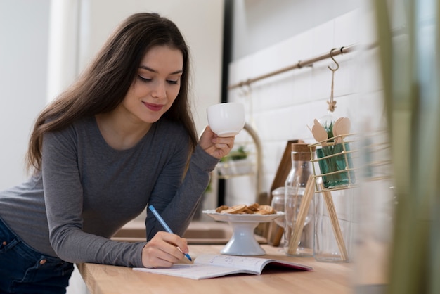 Foto porträt der jungen frau, die notizen beim kaffee macht