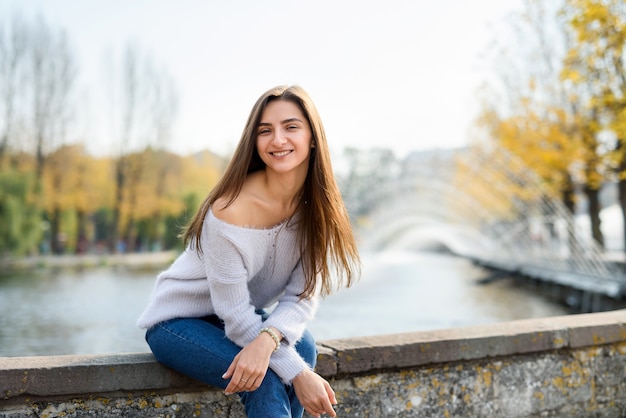 Foto porträt der jungen frau in der freizeitkleidung, die nahe brunnen im freien aufwirft